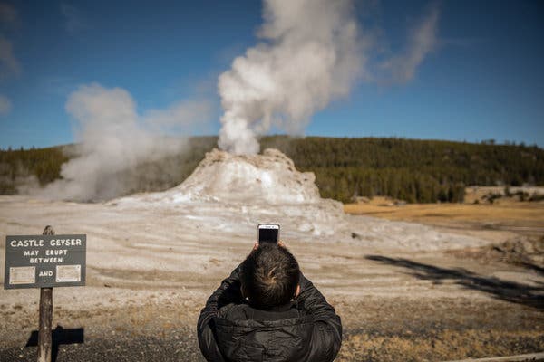 A tourist taking photographs of Castle Geyser at Yellowstone National Park in 2018.
